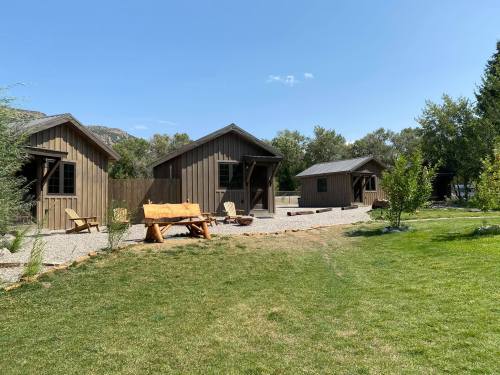 Three rustic cabins surrounded by greenery and gravel paths under a clear blue sky.