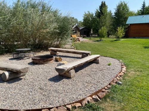 A cozy outdoor fire pit area with log benches, surrounded by gravel and greenery, under a clear blue sky.