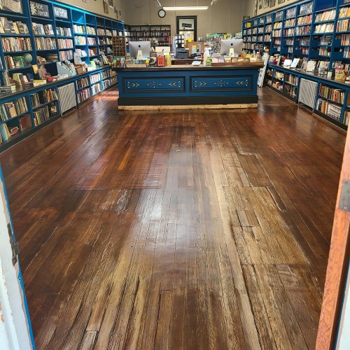 A cozy bookstore interior with wooden floors, shelves filled with books, and a central checkout counter.