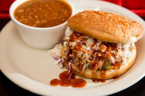 A sesame seed bun filled with pulled pork and coleslaw, served with a side of baked beans.