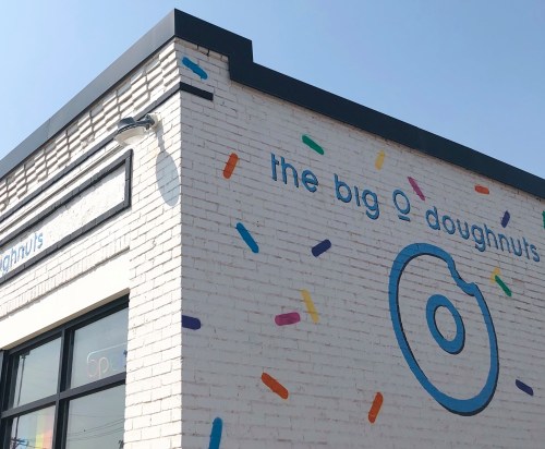 Exterior of a doughnut shop with colorful sprinkles and the name "the big O doughnuts" on a white brick wall.