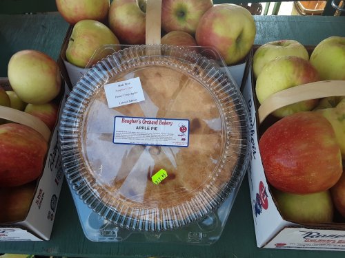 A freshly baked apple pie on a table, surrounded by baskets of shiny red apples.