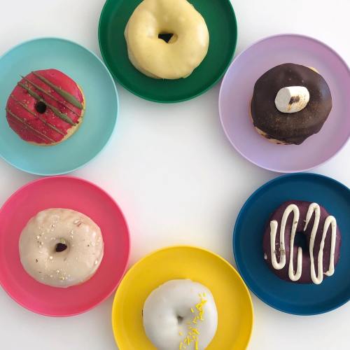 A colorful arrangement of six donuts on pastel plates, featuring various toppings and flavors.