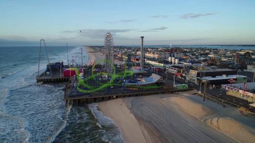 Aerial view of a beach amusement park with rides, a pier, and the ocean in the background during sunset.