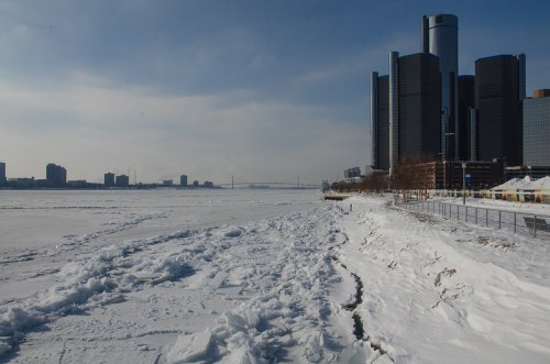 A frozen river with ice formations, flanked by modern buildings under a clear sky.