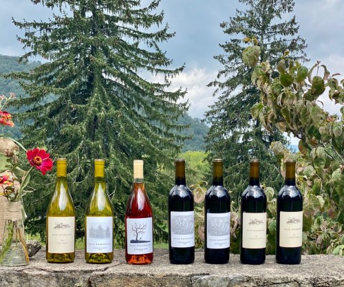 A selection of wines displayed on a stone ledge, with lush greenery and cloudy skies in the background.