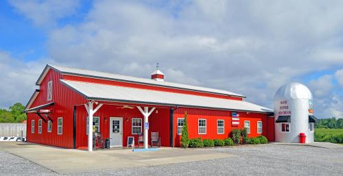 A red barn-style building with a white roof and a round ice cream stand nearby, set against a cloudy blue sky.