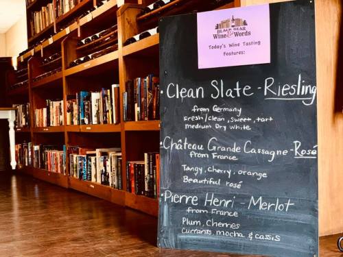 Chalkboard listing today's wine tasting features: Riesling, Rosé, and Merlot, with descriptions, in a cozy wine shop.