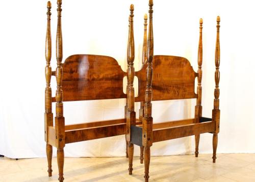 Two wooden bed frames with tall, turned posts and a rich finish, positioned back to back against a white background.