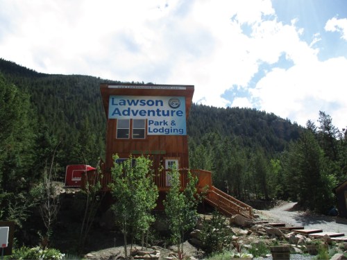 A wooden lodge with a sign reading "Lawson Adventure Park & Lodging," surrounded by trees and mountains.