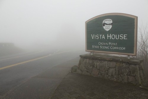 Foggy scene featuring a sign for Vista House at Crown Point State Scenic Corridor in Oregon.