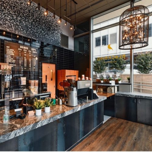 A modern coffee shop interior featuring a marble counter, menu board, and stylish lighting fixtures.