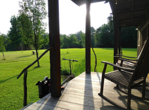 A peaceful porch view with rocking chairs overlooking a green lawn and trees in the background, bathed in soft sunlight.