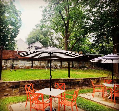A cozy outdoor patio with striped umbrellas, orange chairs, and a grassy area surrounded by trees and a wooden fence.