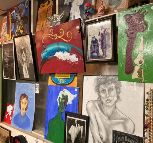 A collage of various artworks, including portraits and abstract pieces, displayed on a wall in a gallery.