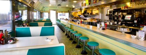 A retro diner interior featuring teal booths, a long counter, and a classic checkered floor.