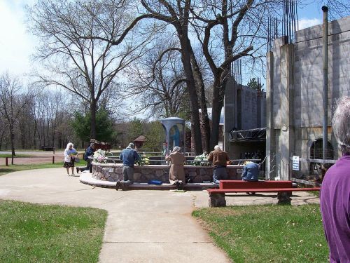 A group of people working on a stone fountain in a park, surrounded by trees and a partially constructed building.