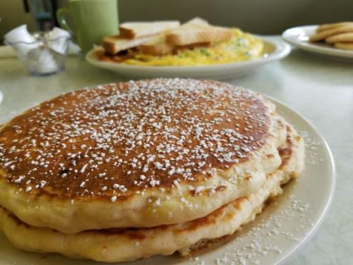 A close-up of fluffy pancakes dusted with powdered sugar, with toast and an omelet in the background.