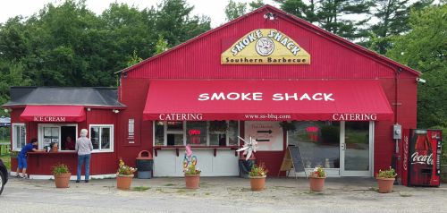 A red building with "Smoke Shack" signage, featuring an ice cream stand and outdoor seating, surrounded by potted plants.
