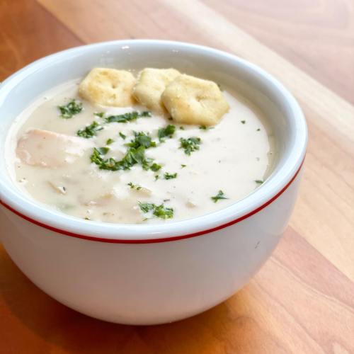 A bowl of creamy soup topped with herbs and crackers, placed on a wooden table.