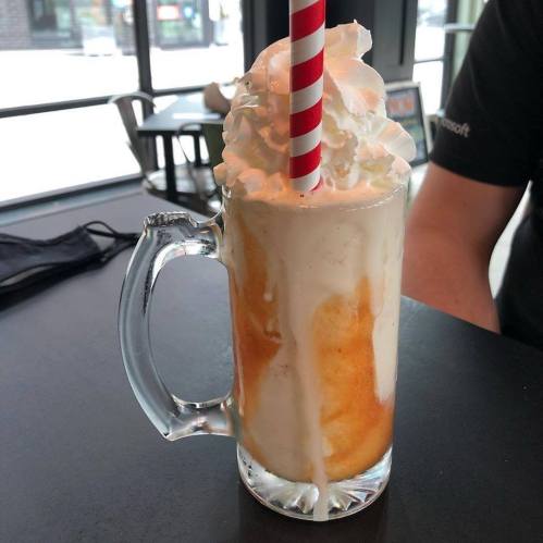 A frosty mug filled with a creamy orange drink topped with whipped cream and a red and white striped straw.
