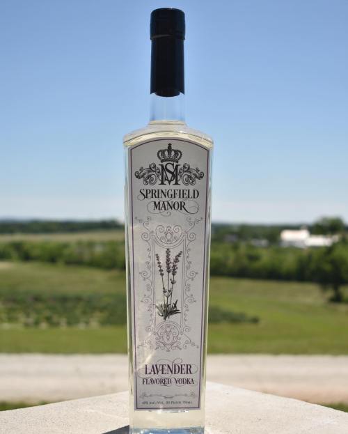A bottle of Springfield Manor Lavender Flavored Vodka against a clear blue sky and green landscape.