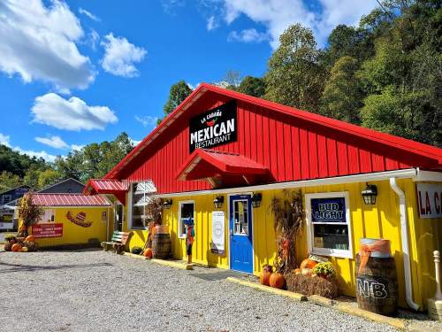 Colorful Mexican restaurant with a red roof and yellow walls, surrounded by autumn decorations and a clear blue sky.