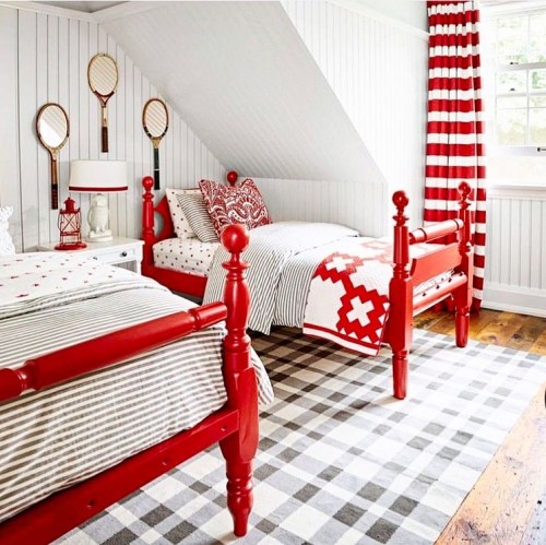 Brightly decorated bedroom with red beds, striped bedding, and red and white curtains, featuring a checkered rug.