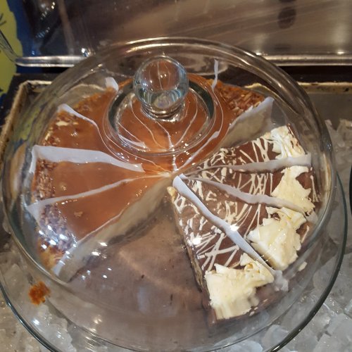 A glass dome covers a cake with two distinct flavors: caramel and chocolate, each with decorative icing.