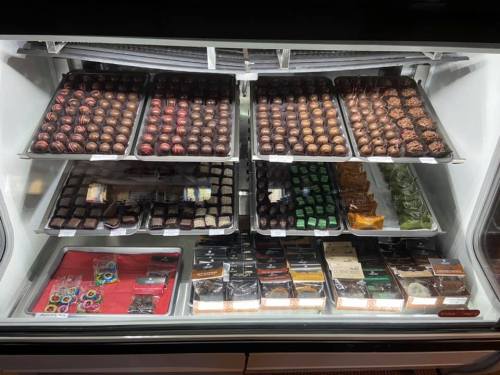 A display case filled with various chocolates and confections, neatly arranged on trays.