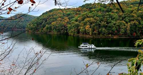 A boat glides through a calm lake surrounded by colorful autumn foliage and lush green hills.