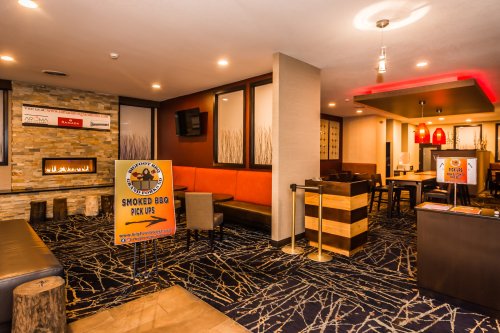 Cozy restaurant interior with a fireplace, seating areas, and a sign for smoked BBQ pick-ups. Warm lighting and modern decor.
