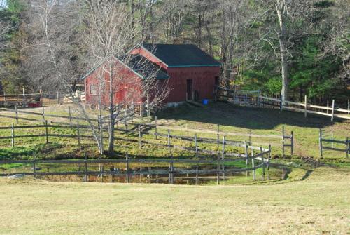A red barn surrounded by a wooden fence, with a small pond and trees in a grassy field.