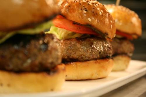 Three delicious burgers with sesame seed buns, lettuce, and tomato, arranged on a white plate.