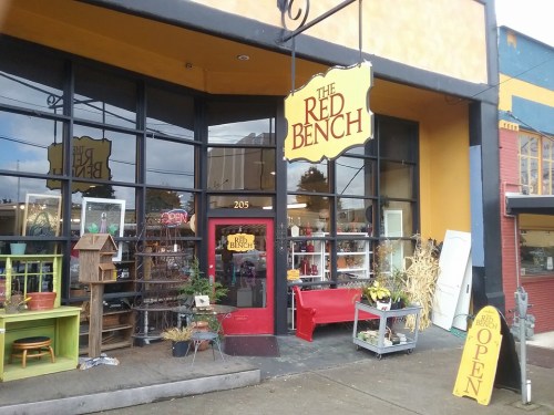 Exterior of "The Red Bench" store, featuring large windows, a red door, and a colorful sign indicating it's open.