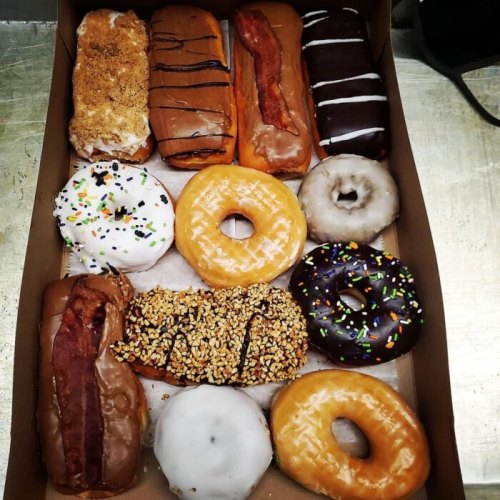A box of assorted donuts, including glazed, chocolate, and bacon-topped varieties, arranged neatly.