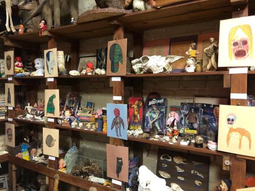 A cluttered shelf filled with eclectic items, including art, toys, and curiosities, creating a whimsical display.