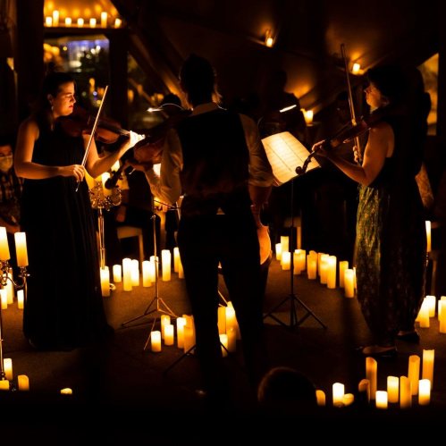 A string trio performs in a dimly lit space surrounded by glowing candles, creating an intimate atmosphere.