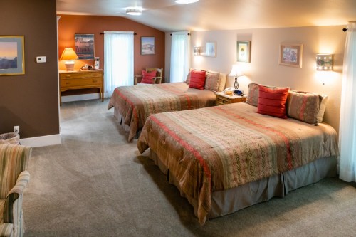 Cozy hotel room with two beds, warm lighting, and a dresser, featuring soft decor and a welcoming atmosphere.