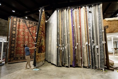 A person examines a large display of colorful rugs in a showroom, showcasing various patterns and textures.
