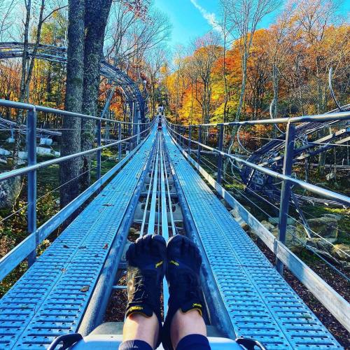 A view from a mountain coaster track, with feet in minimalist shoes and colorful autumn trees in the background.
