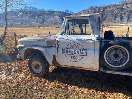 A vintage truck with rust and a "Basecamp 550" logo parked in a scenic, mountainous landscape.