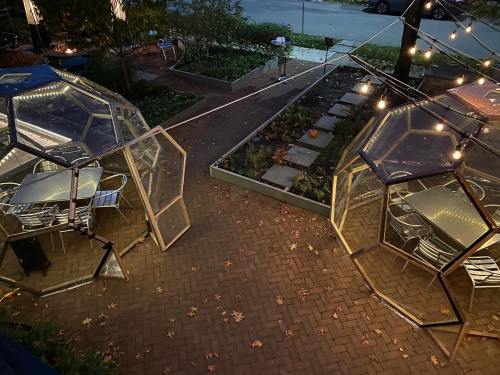 Two transparent geodesic dining pods with string lights, surrounded by a garden and fallen leaves on a brick pathway.