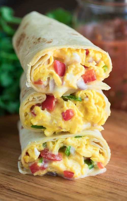 Three rolled tortillas filled with scrambled eggs, diced tomatoes, and green onions, stacked on a wooden surface.