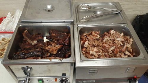 Two metal trays filled with cooked meats: one with ribs and the other with shredded pork, served in a buffet style.