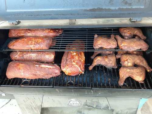 A smoker filled with various meats, including ribs and chicken, cooking over a charcoal grill.