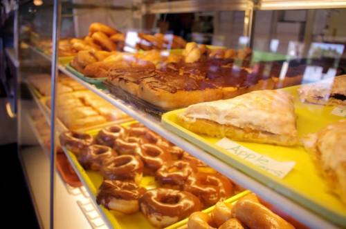 A display case filled with various pastries, including donuts and apple turnovers, arranged on yellow trays.