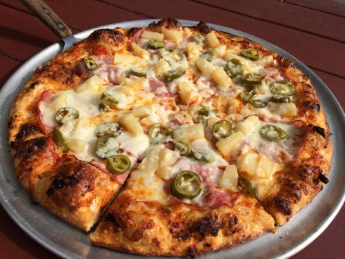 A freshly baked pizza topped with ham, pineapple, jalapeños, and melted cheese on a golden crust.