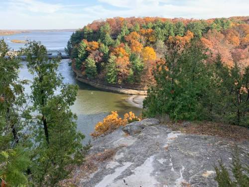 A scenic view of a river curving through autumn-colored trees and rocky cliffs under a clear sky.