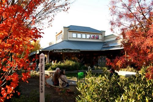 A cozy food cooperative surrounded by vibrant autumn foliage, with people sitting on a bench outside.